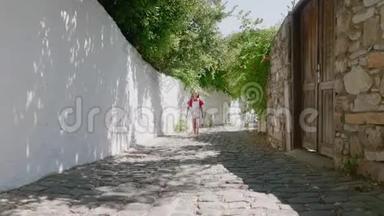在旧城狭窄的街道上散步的女孩。 旅游女孩走在阳光明媚的街道上，岩石墙背景，夏天的老人